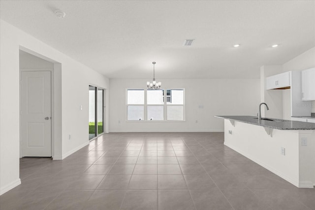 kitchen featuring hanging light fixtures, white cabinets, dark stone countertops, a notable chandelier, and a breakfast bar area