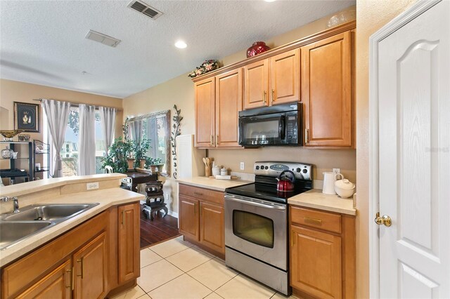 kitchen featuring stainless steel range with electric stovetop, a textured ceiling, sink, and light tile patterned flooring