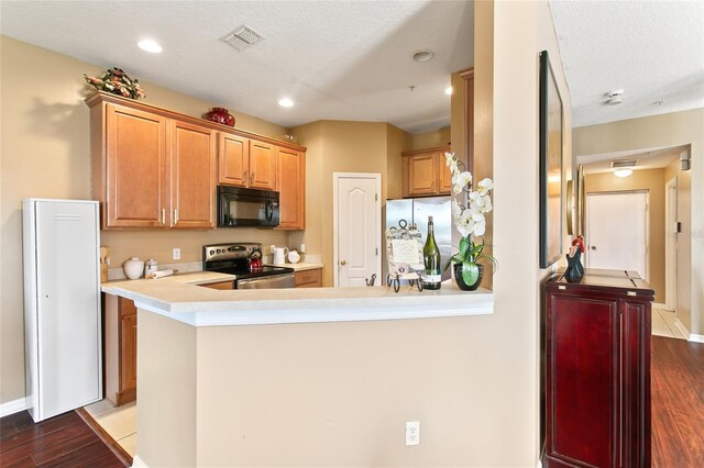 kitchen with kitchen peninsula, a textured ceiling, appliances with stainless steel finishes, and dark wood-type flooring