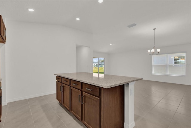 kitchen featuring a kitchen island, light tile patterned flooring, pendant lighting, a chandelier, and light stone counters