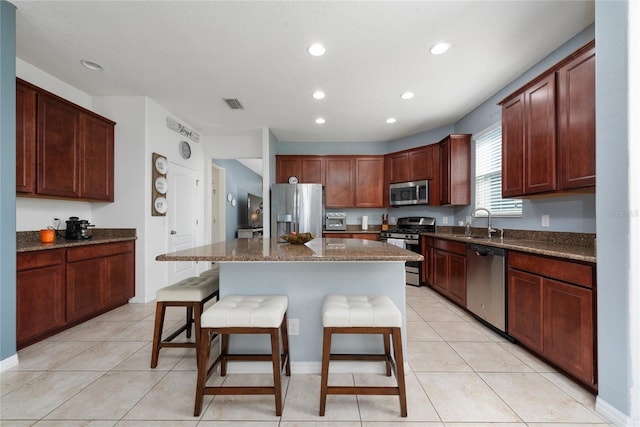 kitchen featuring dark stone counters, a kitchen breakfast bar, sink, appliances with stainless steel finishes, and a kitchen island