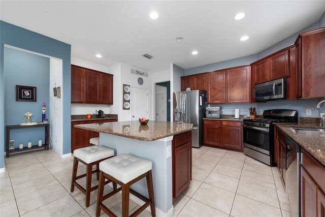 kitchen featuring sink, stainless steel appliances, a kitchen breakfast bar, dark stone countertops, and a kitchen island