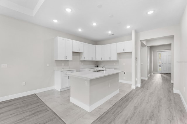 kitchen with white cabinets, light wood-type flooring, sink, and a kitchen island with sink