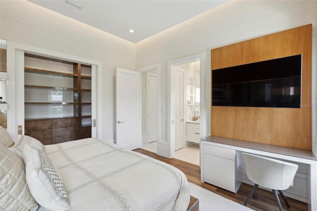 bedroom with ensuite bath, built in desk, and wood-type flooring