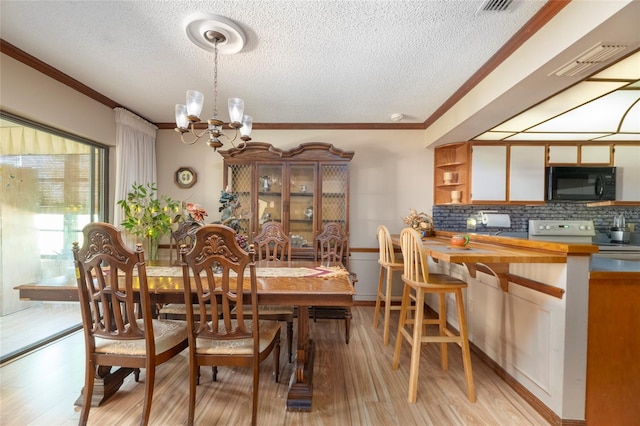 dining room featuring light hardwood / wood-style floors, a textured ceiling, an inviting chandelier, and crown molding