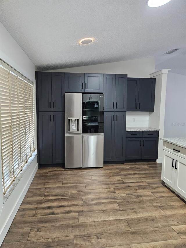 kitchen featuring hardwood / wood-style floors, white cabinetry, a textured ceiling, stainless steel fridge, and vaulted ceiling