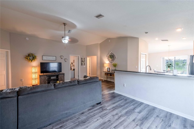 living area featuring lofted ceiling, visible vents, baseboards, and wood finished floors