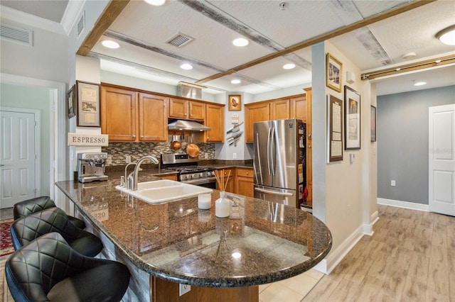 kitchen with appliances with stainless steel finishes, a kitchen bar, sink, light wood-type flooring, and kitchen peninsula