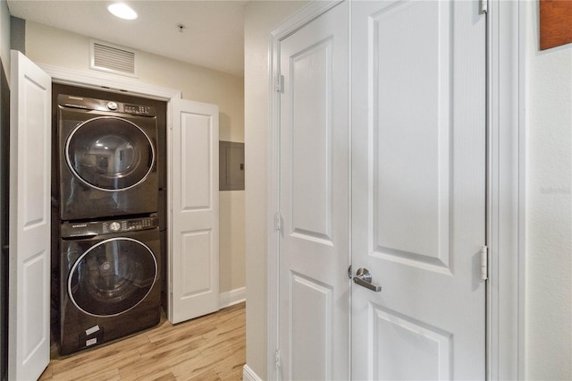 clothes washing area with light wood-type flooring, stacked washer and dryer, and electric panel