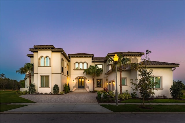 mediterranean / spanish home with driveway, french doors, a tiled roof, a yard, and stucco siding