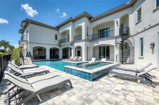 back of property with a balcony, a patio, and a pool with hot tub