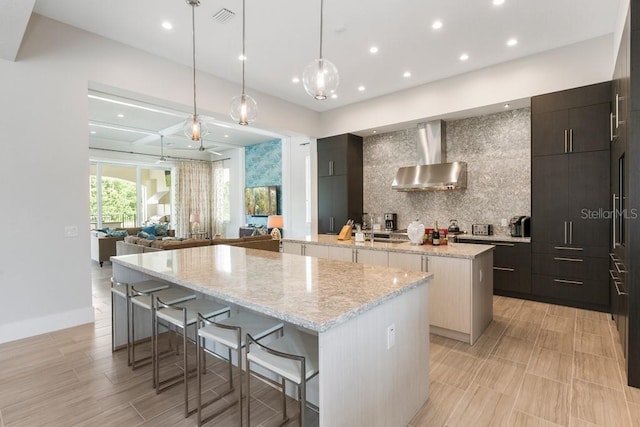 kitchen with wall chimney exhaust hood, tasteful backsplash, dark brown cabinetry, and a kitchen island