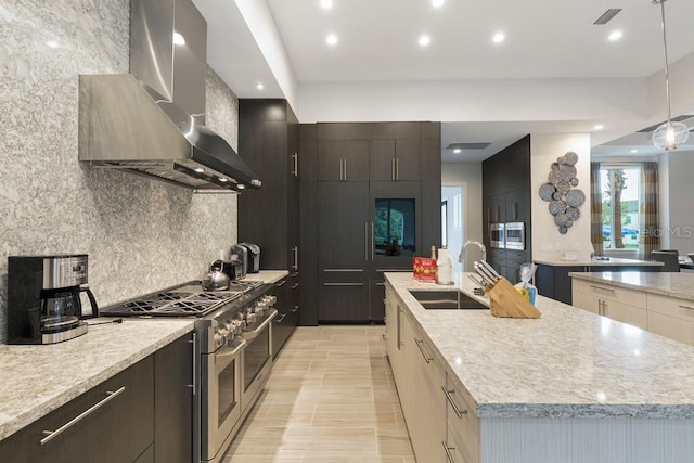 kitchen featuring wall chimney exhaust hood, an island with sink, double oven range, light stone countertops, and sink