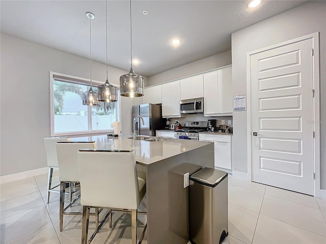 kitchen with pendant lighting, appliances with stainless steel finishes, an island with sink, white cabinetry, and light tile patterned flooring