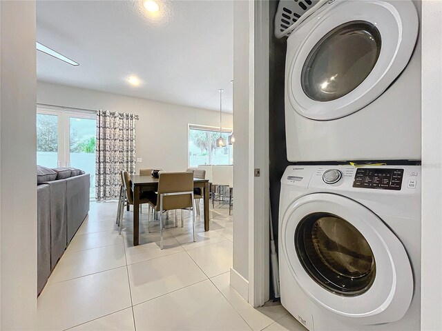 laundry room with a notable chandelier, light tile patterned floors, and stacked washer and dryer