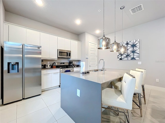 kitchen with hanging light fixtures, stainless steel appliances, white cabinetry, sink, and a breakfast bar area