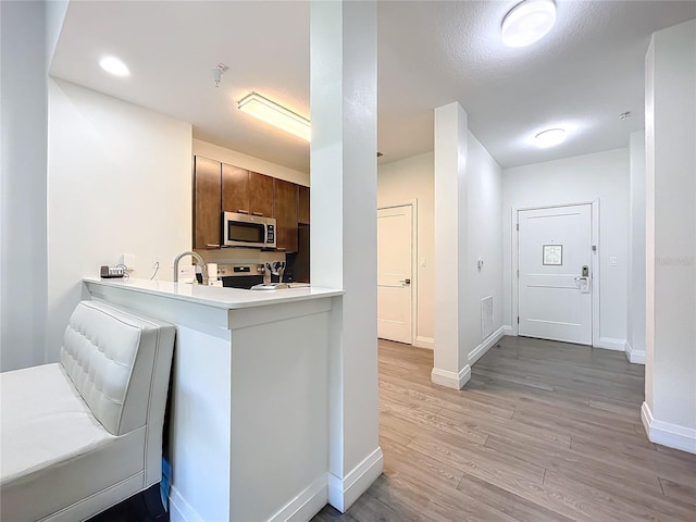 kitchen featuring light wood finished floors, light countertops, stainless steel microwave, a peninsula, and baseboards