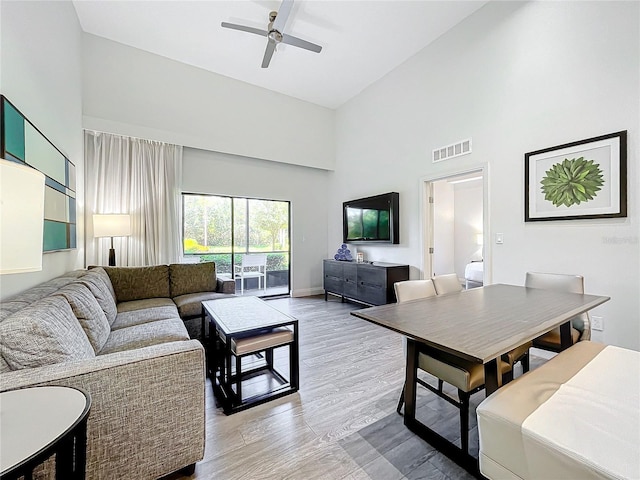 living area featuring ceiling fan, high vaulted ceiling, visible vents, baseboards, and light wood-style floors