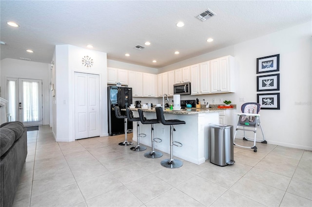 kitchen featuring white cabinetry, a kitchen bar, stone countertops, black fridge with ice dispenser, and light tile patterned flooring