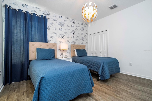 bedroom featuring a chandelier, wood finished floors, visible vents, baseboards, and a closet