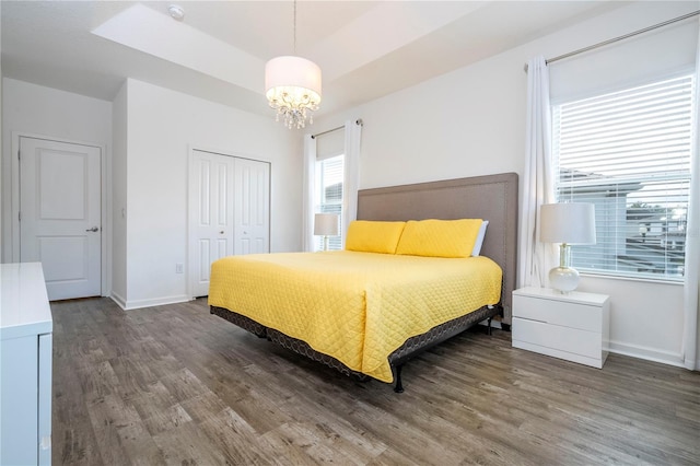 bedroom featuring a closet, a raised ceiling, an inviting chandelier, and hardwood / wood-style flooring