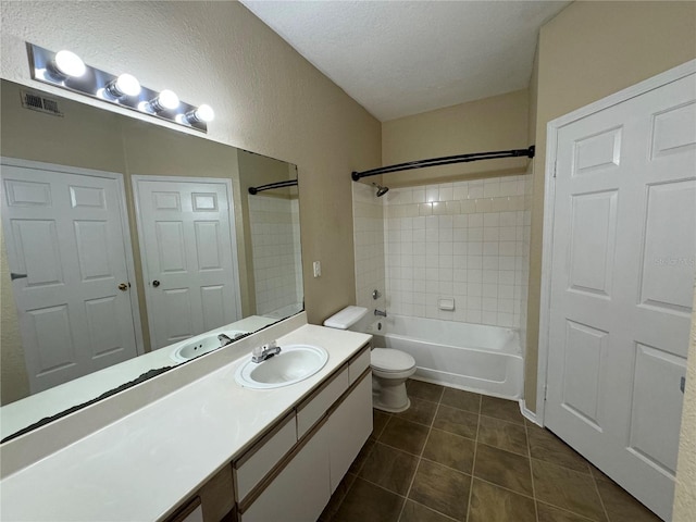 full bathroom featuring toilet, vanity, tile patterned floors, a textured ceiling, and tiled shower / bath