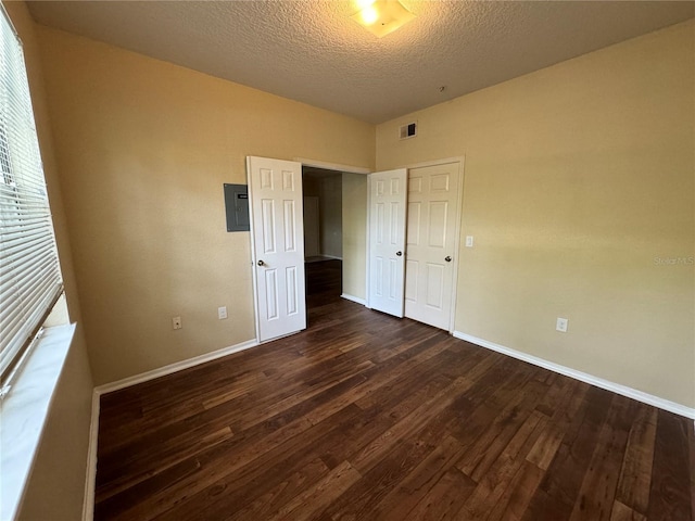 unfurnished bedroom with dark hardwood / wood-style floors, a textured ceiling, and electric panel