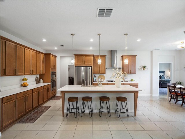 kitchen with a kitchen island with sink, pendant lighting, appliances with stainless steel finishes, a breakfast bar area, and wall chimney range hood