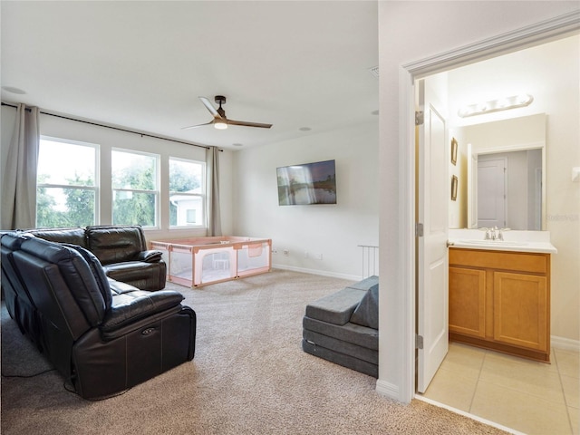 living area featuring light carpet, light tile patterned floors, a ceiling fan, and baseboards