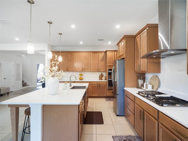 kitchen featuring hanging light fixtures, stainless steel appliances, sink, wall chimney range hood, and a kitchen bar