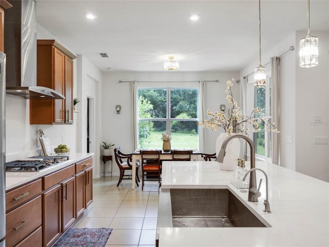 kitchen with stainless steel gas cooktop, decorative light fixtures, light tile patterned floors, sink, and wall chimney exhaust hood