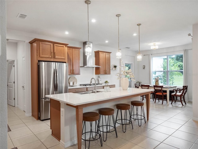 kitchen with visible vents, an island with sink, freestanding refrigerator, light countertops, and wall chimney range hood