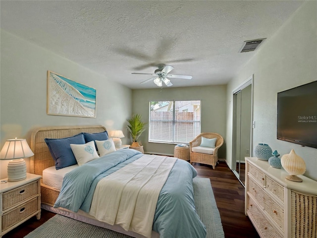 bedroom with visible vents, dark wood finished floors, a closet, a textured ceiling, and a ceiling fan