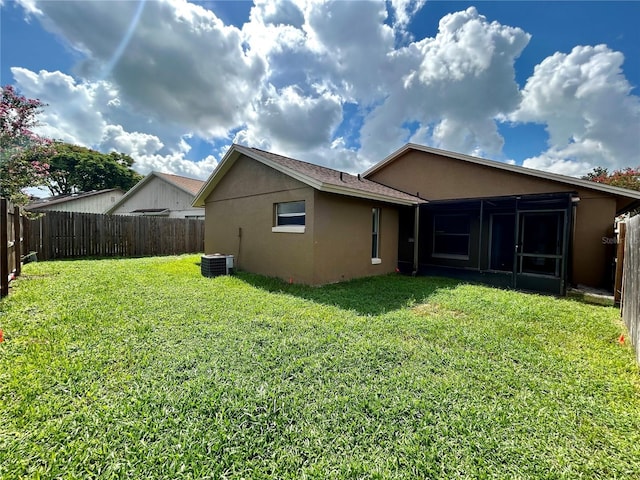 rear view of property featuring stucco siding, a lawn, a fenced backyard, and a sunroom