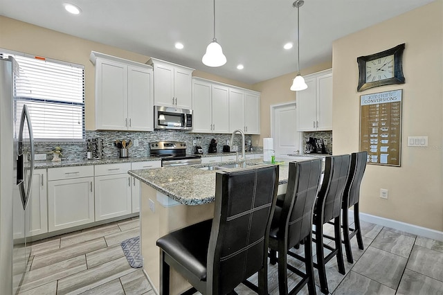 kitchen featuring white cabinetry, appliances with stainless steel finishes, light stone countertops, and backsplash