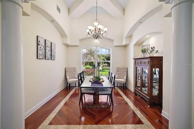 dining area featuring a towering ceiling, a notable chandelier, ornate columns, and dark hardwood / wood-style flooring