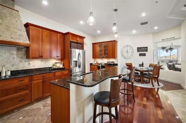 kitchen featuring hanging light fixtures, an island with sink, dark wood-type flooring, stainless steel refrigerator with ice dispenser, and black cooktop