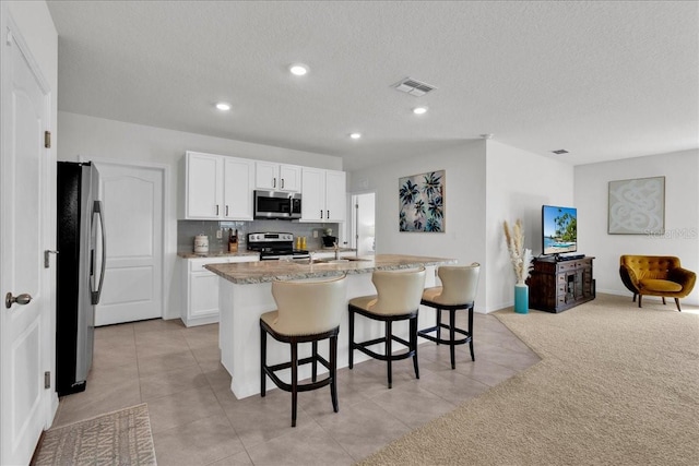 kitchen featuring stainless steel appliances, a center island with sink, white cabinetry, and light carpet