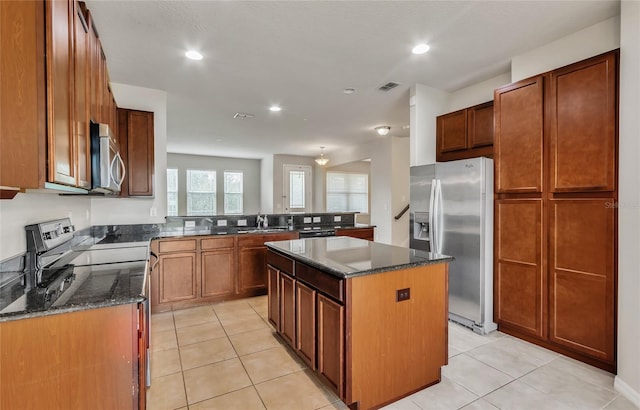 kitchen with a center island, light tile patterned floors, stainless steel appliances, and dark stone counters