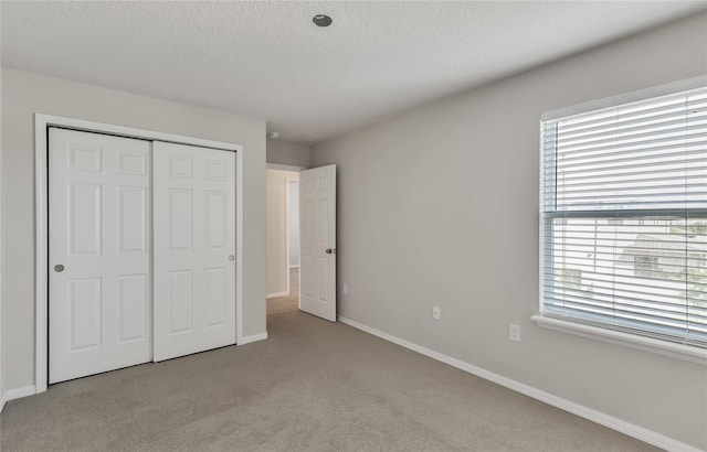 unfurnished bedroom featuring a textured ceiling, a closet, and light carpet