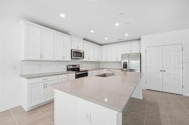 kitchen with white cabinets, stainless steel appliances, a center island with sink, and light tile patterned floors