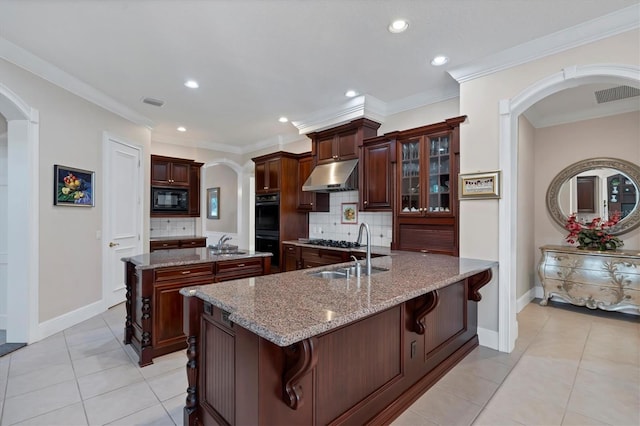 kitchen featuring tasteful backsplash, a kitchen bar, light stone countertops, sink, and black appliances