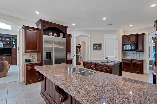 kitchen with a kitchen island with sink, built in appliances, backsplash, and light tile patterned flooring