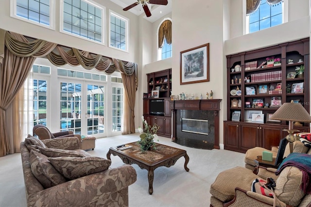 carpeted living room featuring plenty of natural light, ceiling fan, a high end fireplace, and a towering ceiling