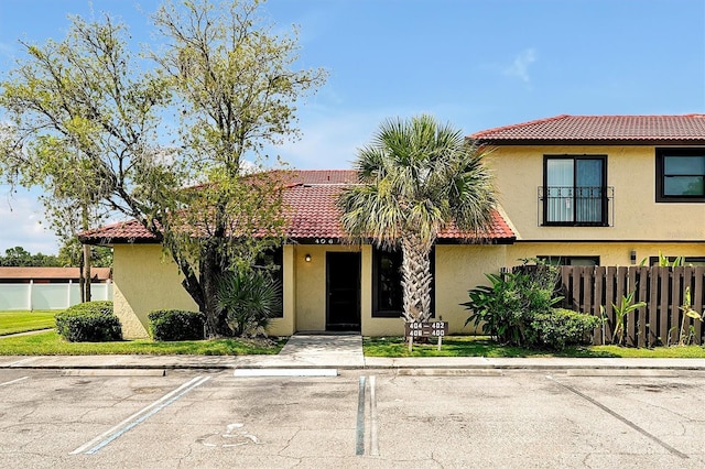 view of front facade featuring a tiled roof, fence, and stucco siding