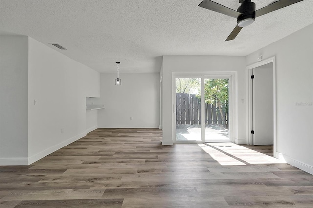 unfurnished living room with baseboards, a textured ceiling, visible vents, and wood finished floors