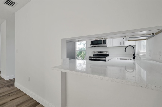 kitchen featuring visible vents, appliances with stainless steel finishes, wood finished floors, light stone countertops, and a sink