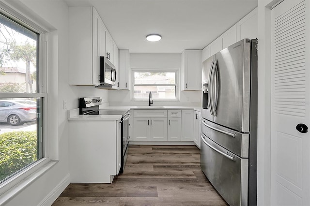 kitchen with light countertops, appliances with stainless steel finishes, dark wood-type flooring, white cabinets, and a sink