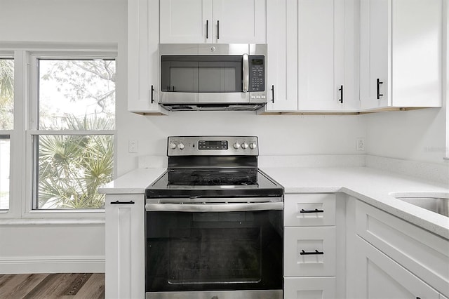 kitchen featuring light stone counters, stainless steel appliances, white cabinetry, wood finished floors, and baseboards