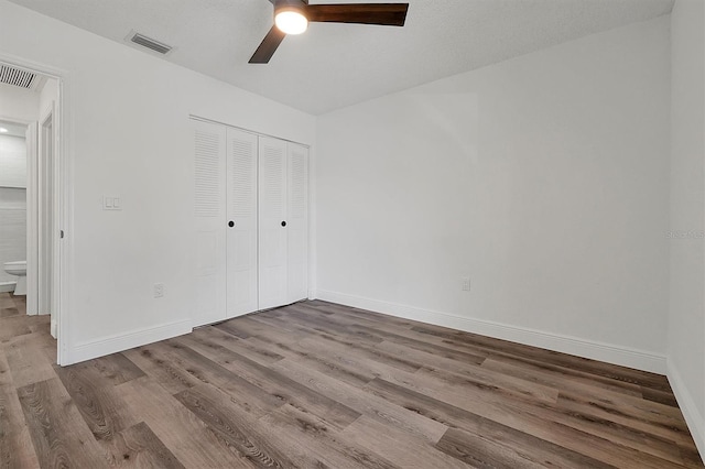 unfurnished bedroom with a closet, visible vents, a ceiling fan, wood finished floors, and baseboards